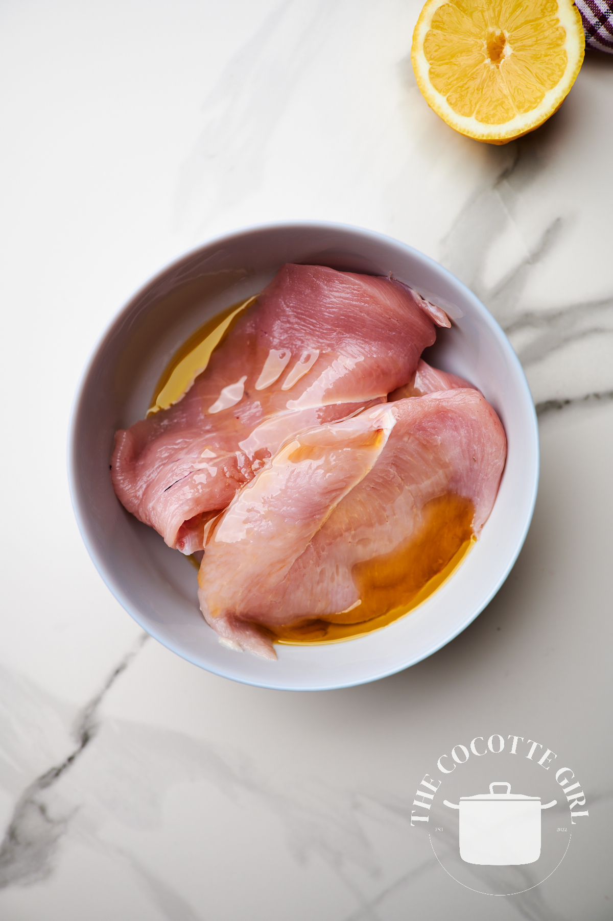 thin chicken breast pieces in a white bowl with olive oil