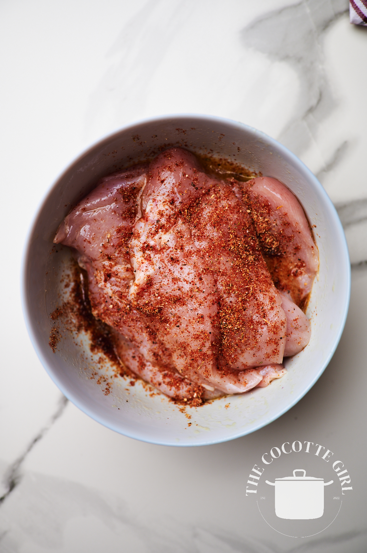 thin chicken breast pieces in a white bowl with the seasonings